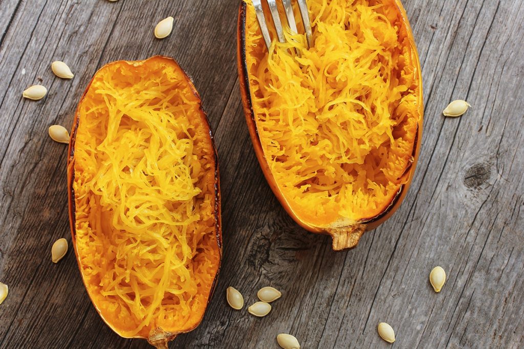 Half cut spaghetti squash top down view with fork placed on top of one half and seeds scattered around