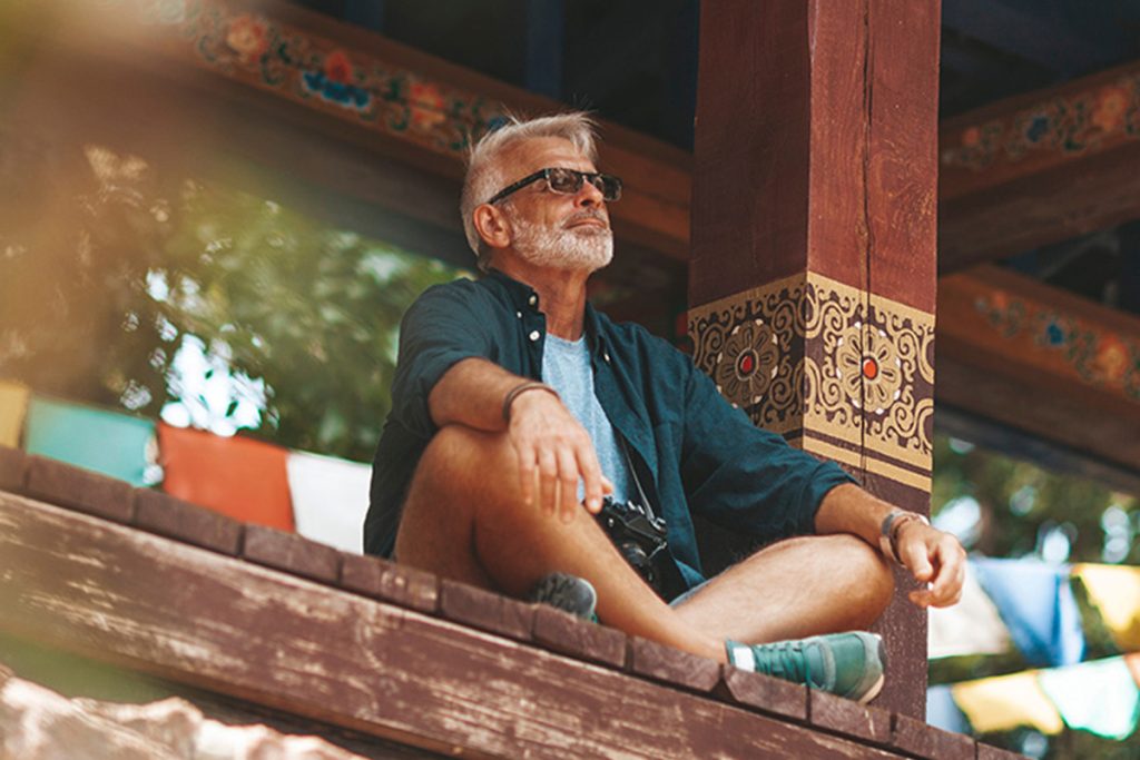 Older man with sunglasses meditating on wooden porch