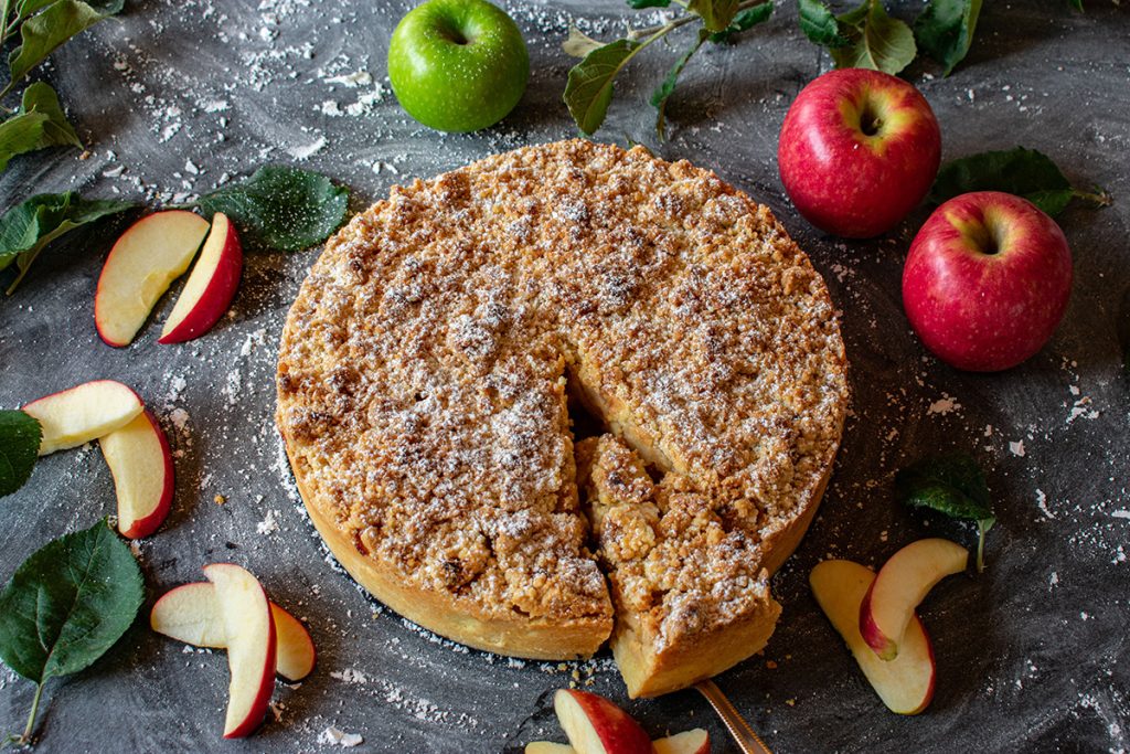 Apple Crumble pie, surrounded by apples and apple slices, with a slice cut out