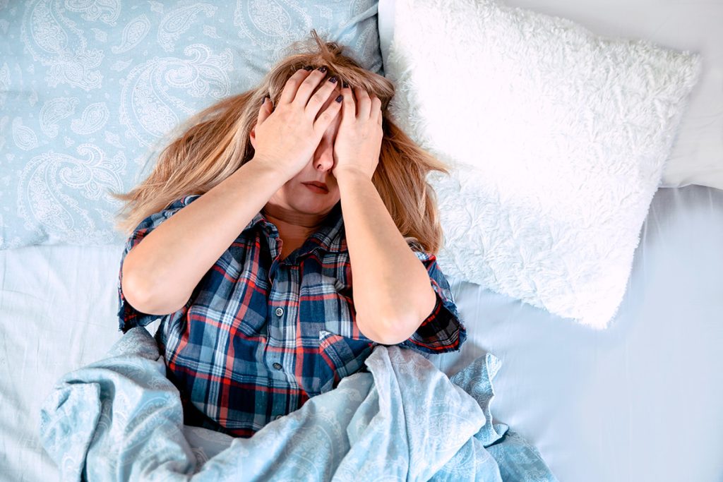 Woman laying in bed with hands covering her hands because she has a migraine