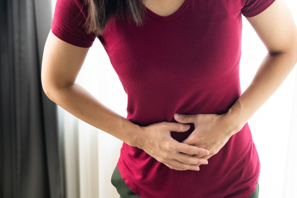 Woman in red shirt, cramping and holding her stomach