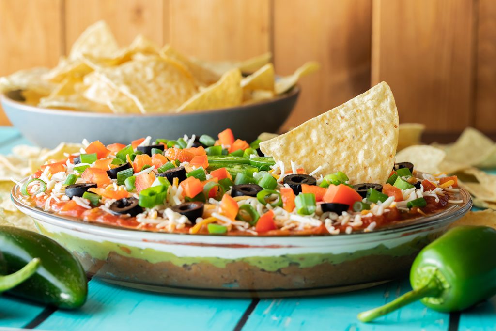 Light Taco dip in a glass pie dish, displayed on a table with green chilis and nachos surrounding it