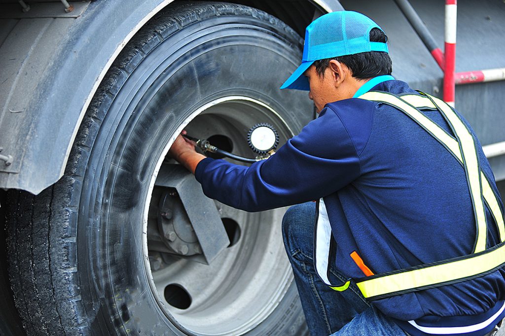 A mechanic in a blue hat pumping the tires of a truck