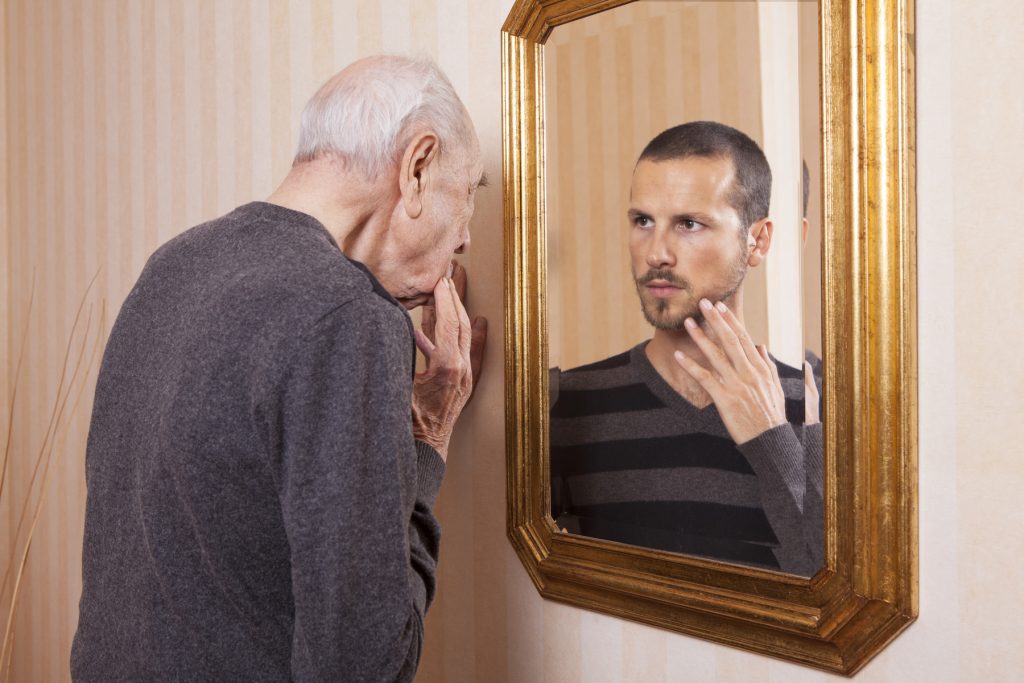 Old man looking in the mirror and seeing his younger self