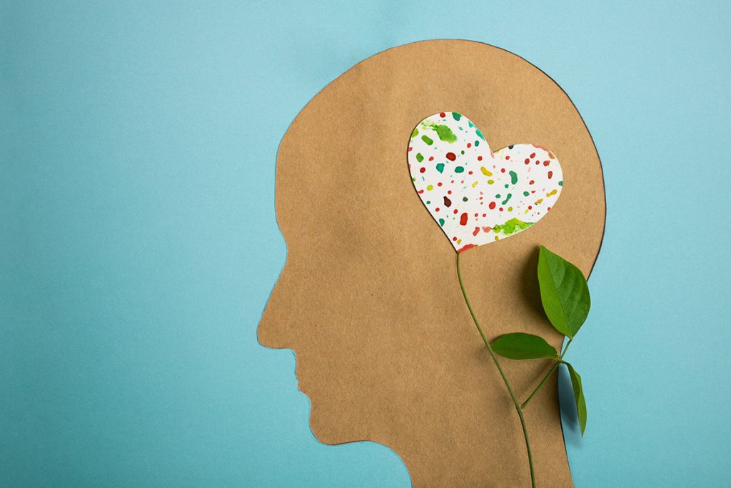 Cut out of a human head silhouette with a heart-shaped brain growing from a flower stem