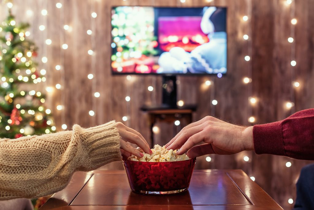 Close up shot of a man and woman's hands grabbing pop corn while watching a holiday movie