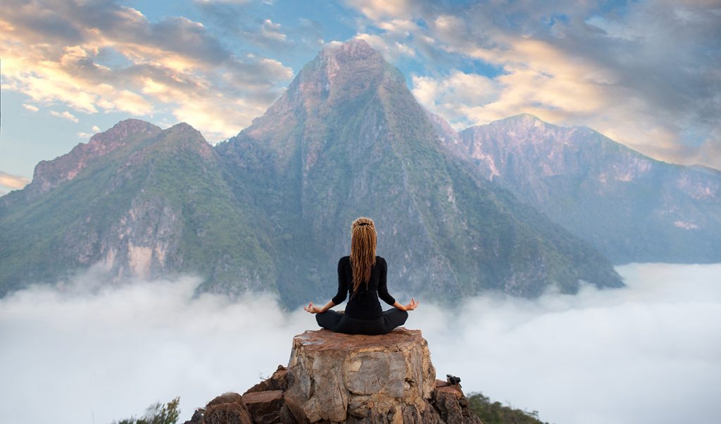 Woman meditating on top of a hill overlooking a beautiful mountainscape