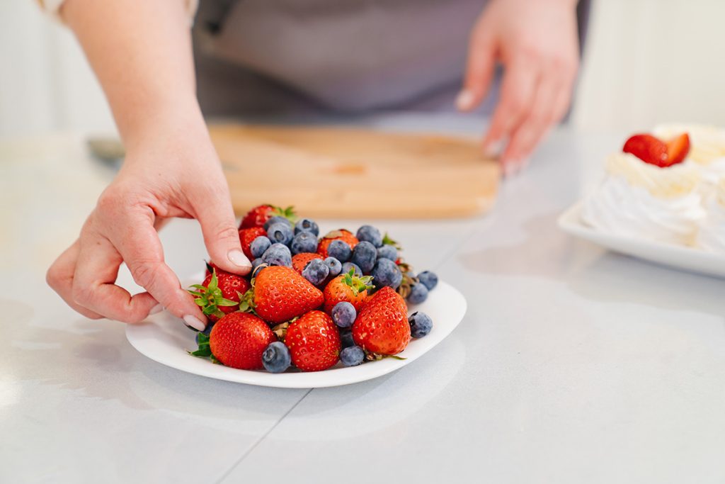 Close up of woman's hand picking up a strawberry from a plate of blueberries and strawberries