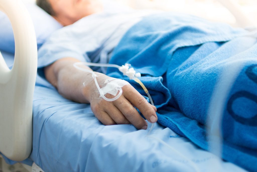 Close up of an IV in a man's hand while he is laying in a hospital bed