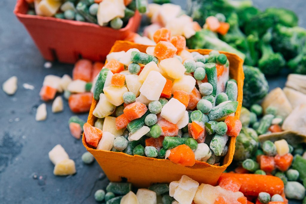 Frozen carrots and peas in a container with frozen broccoli surrounding it