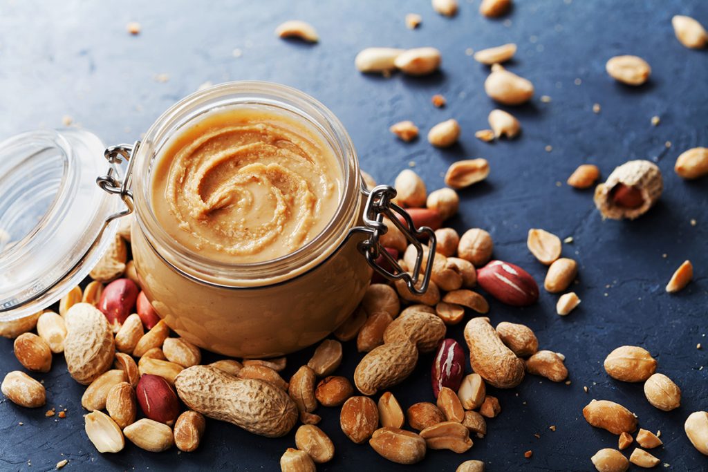 Nut butter in a mason jar with nuts surrounding it
