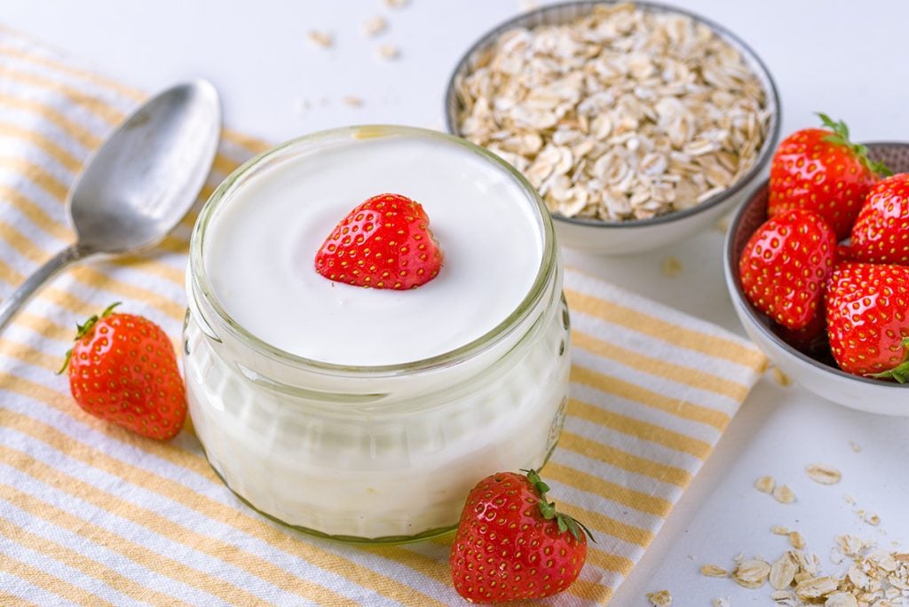 Yogurt with a strawberry in a glass container with oatmeal and strawberries laid next to it
