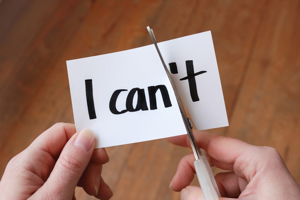 Close up of someone cutting the "'t" off of a card that says "I can't" so that it says "I can"
