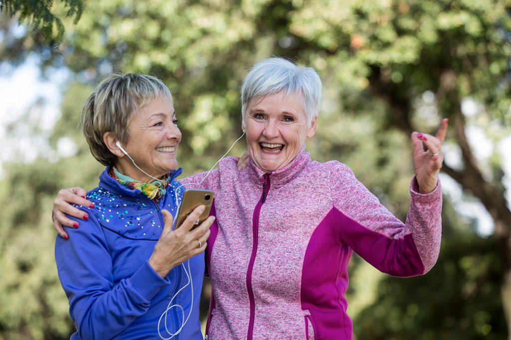 Two older female friends smiling and listening to music