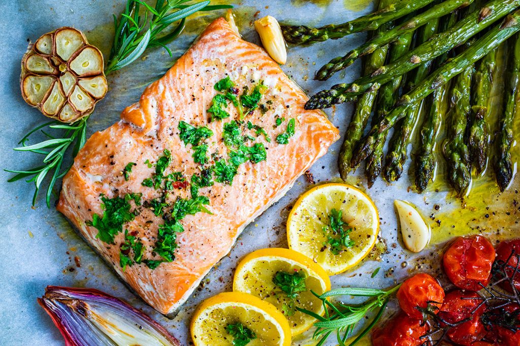 Top view of cooked salmon with cut lemon pieces, asparagus, and other vegetables