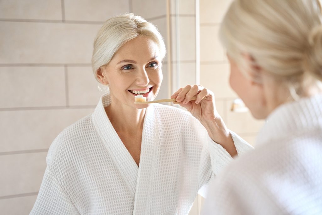 Older woman smiling about to brush her teeth while looking in the mirror