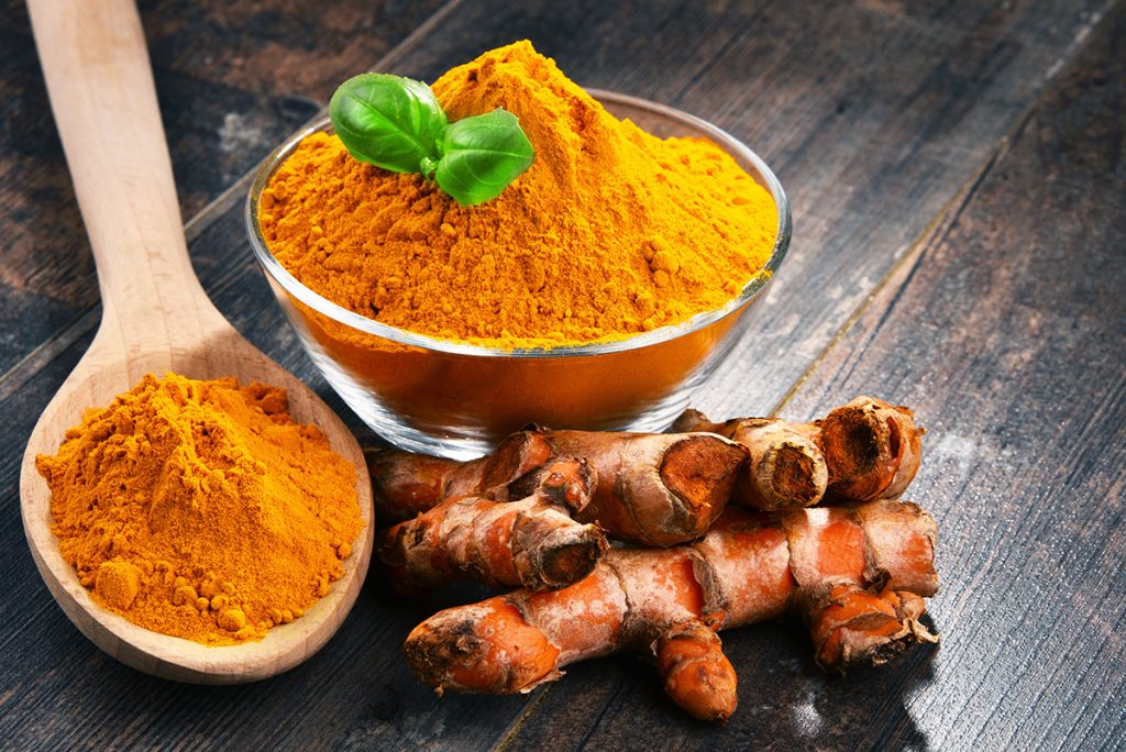 A bowl and spoon full of turmeric powder and ginger on the side