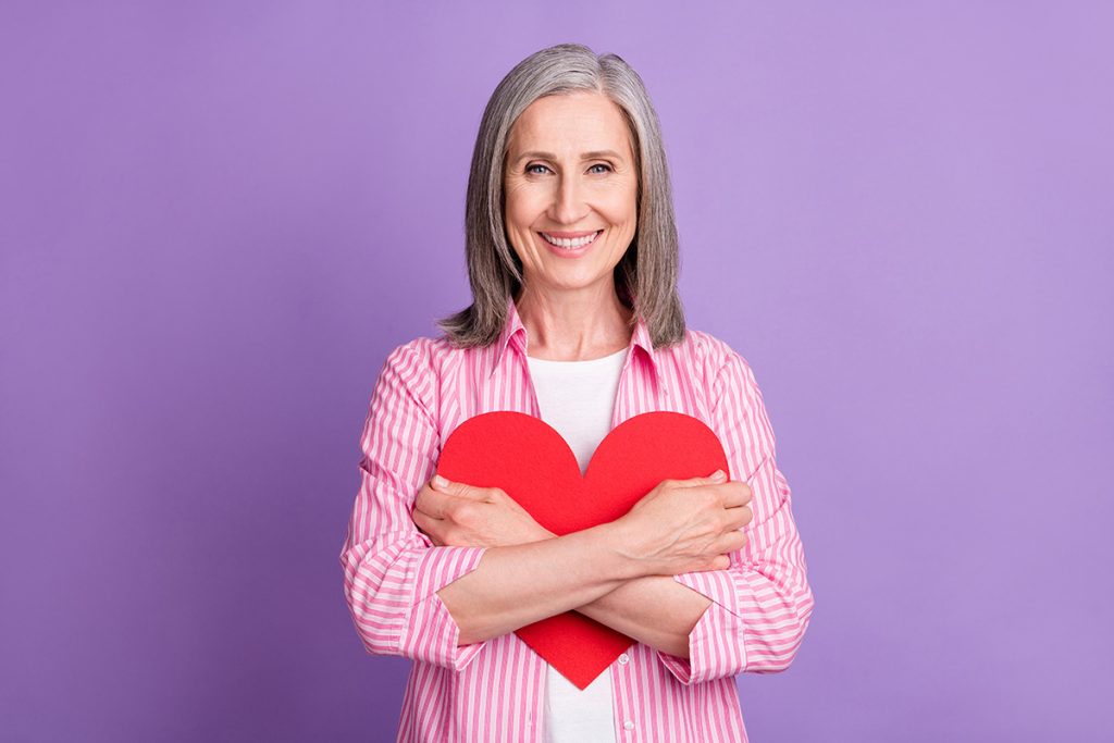 Smiling older woman hugging a paper heart around her chest