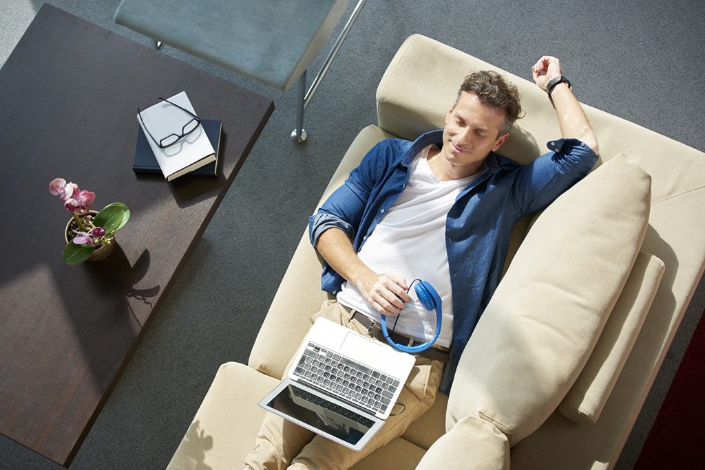 Top view of man resting on the sofa with his laptop and headphones