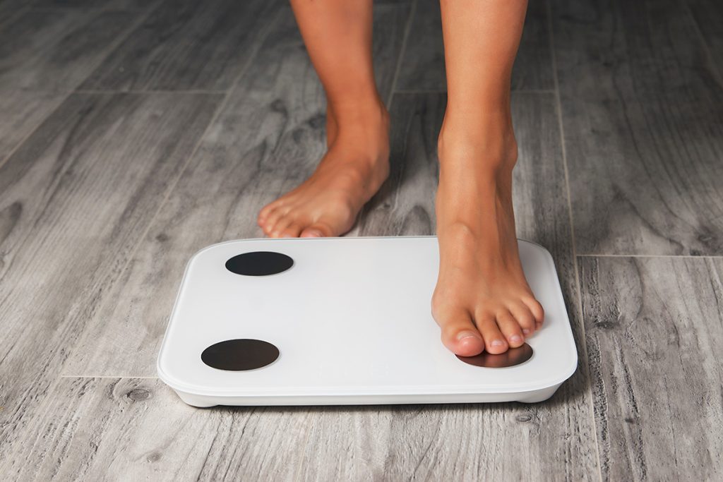 Woman stepping on white body weight scale