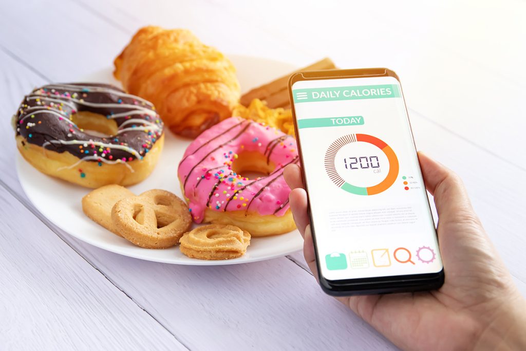 Someone holding up the phone tracking their calories with a plate of donuts in front of them