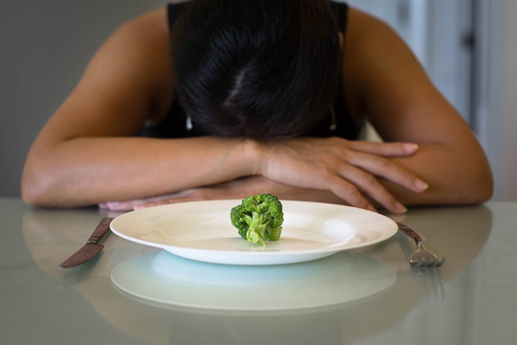 Woman laying in her arms with a single broccoli on a plate in front of her