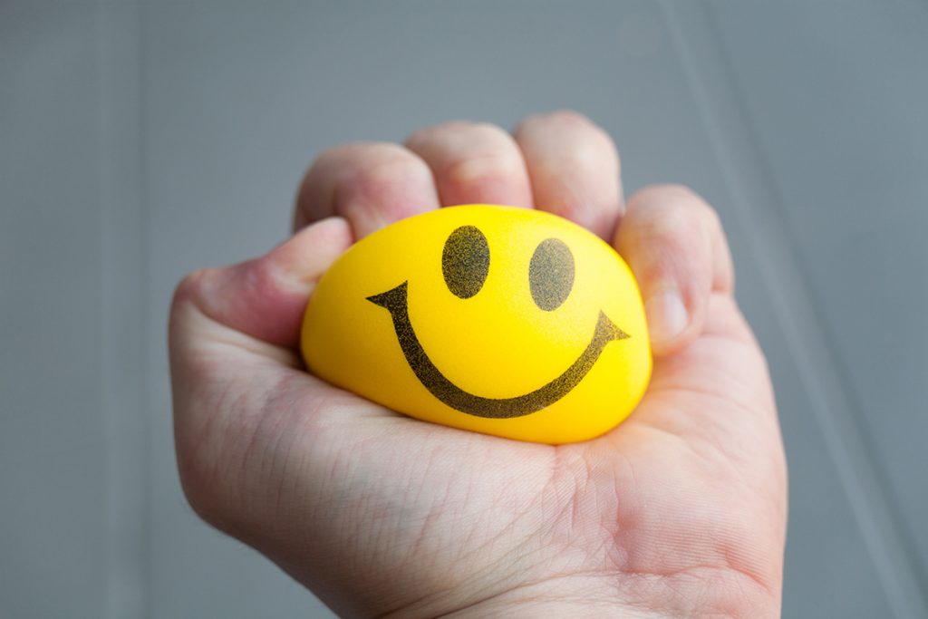 Hand squeezing a stress ball with a smiley face