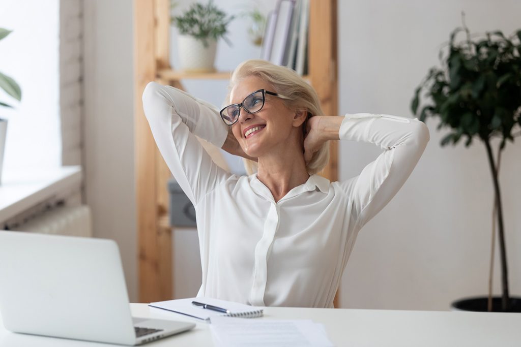 Happy businesswoman with hands behind head relaxing in comfortable office chair during break.