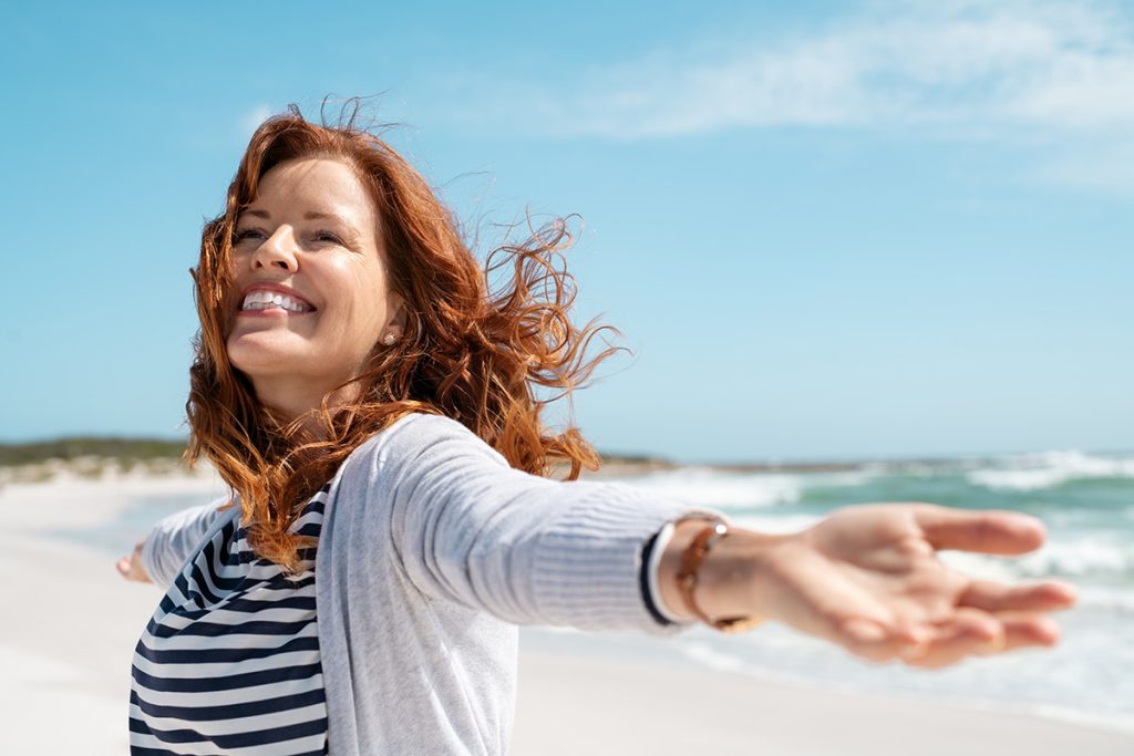 Older woman spreading her arms and  enjoying the breeze and fresh air at the beach