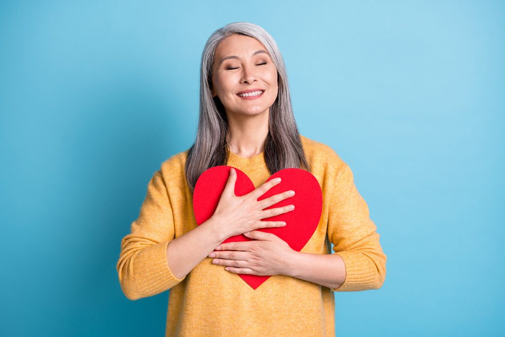 Older woman holding a heart cut out and smiling 