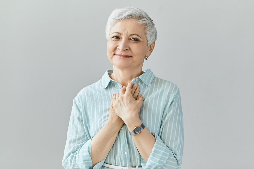 Older woman holding her chest and smiling with gratitude