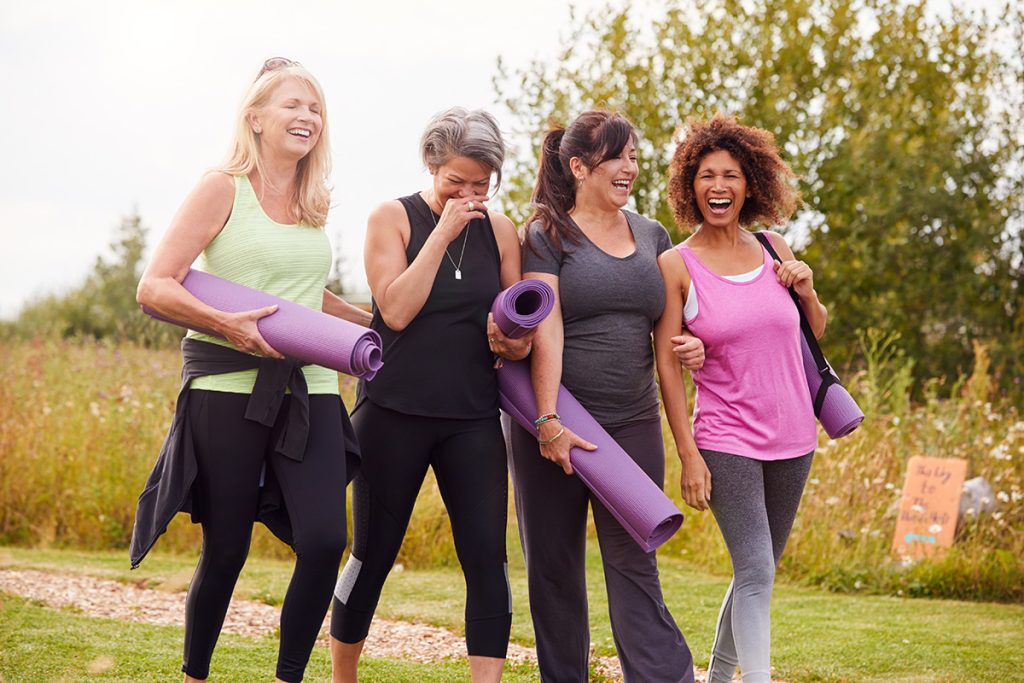 Group of female friends holding yoga mats, walking and laughing