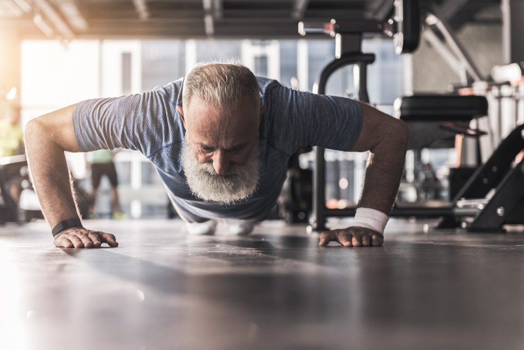 Bearded older man doing push ups in the gym