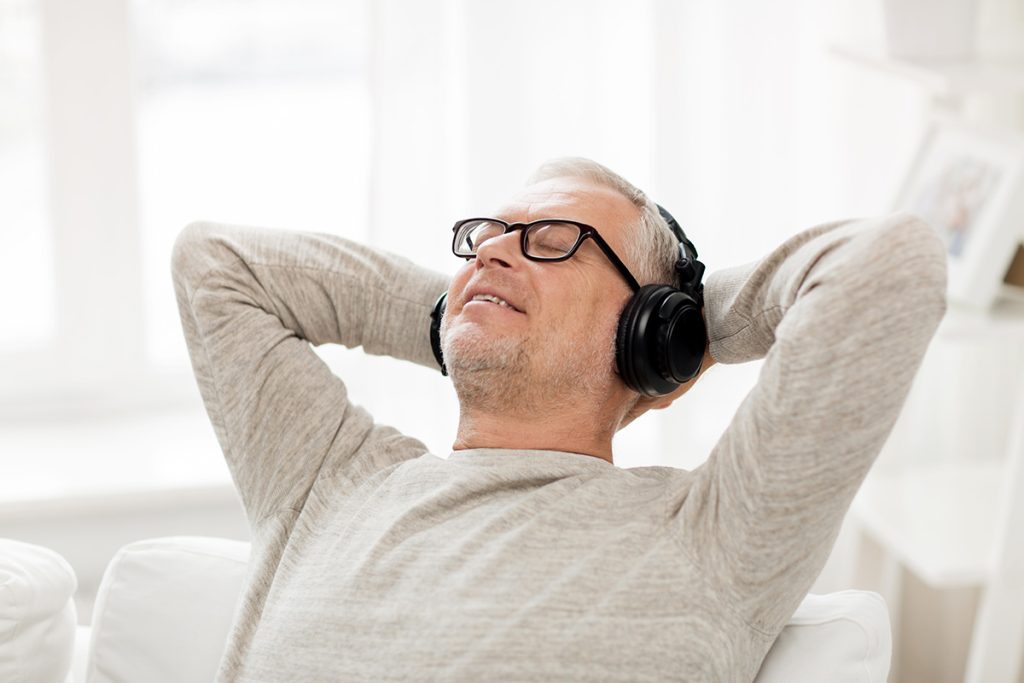 Older man relaxing on couch while listening to music via headphones