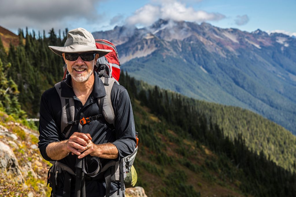 Older man hiking with a view of the mountains in the background