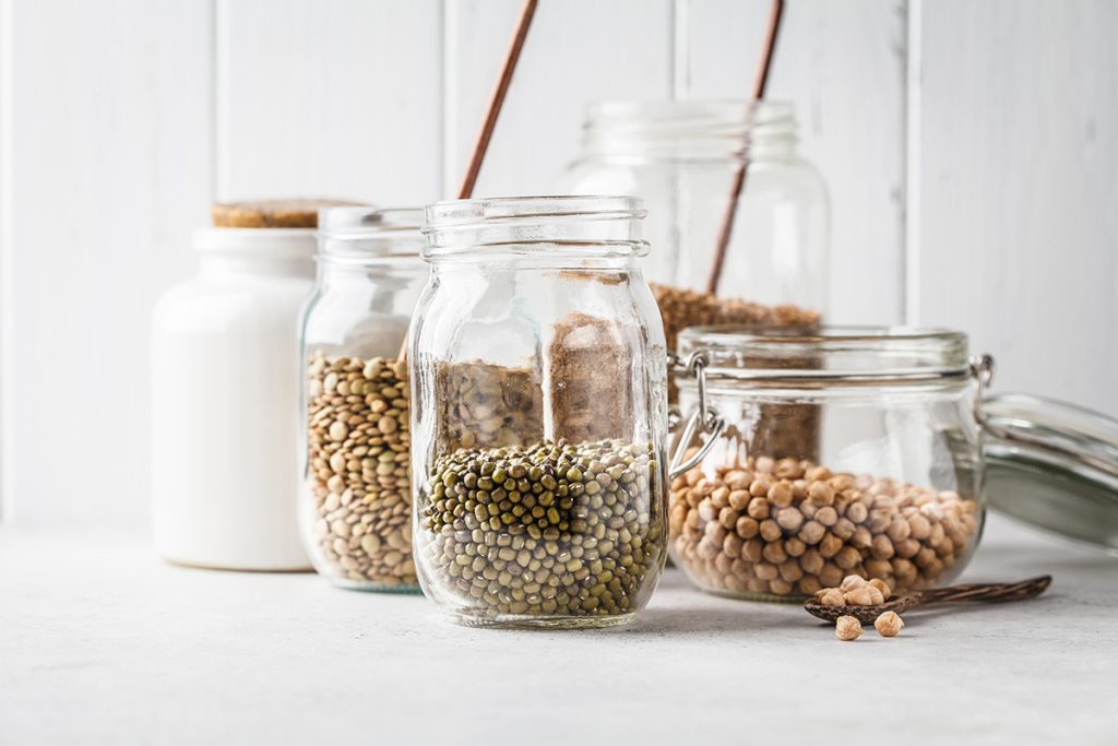 Various legumes: beans, chickpeas, buckwheat, lentils in glass jars on a white background.