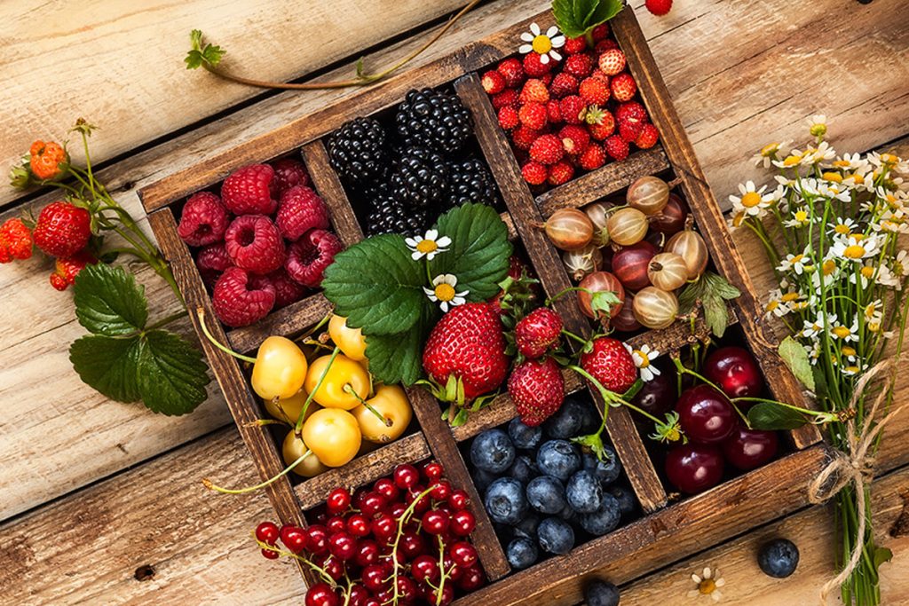 Mix of fresh berries with leaves in vintage wooden box on rustic wooden background. 