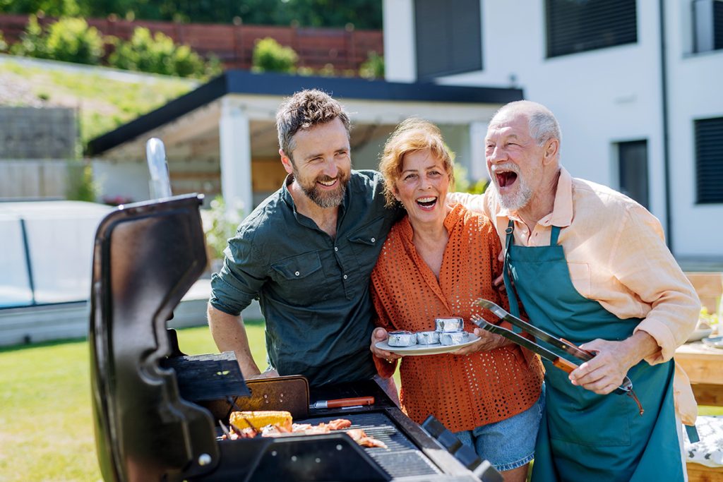 Senior couple with adult son grilling outside on backyard in summer family during garden party