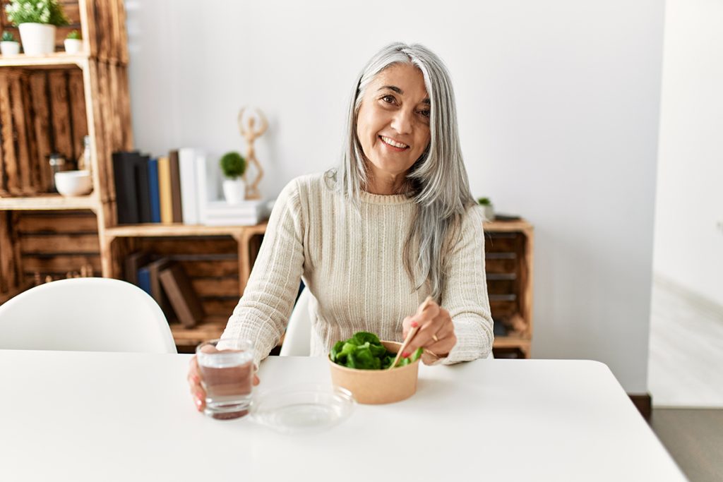 woman smiling eating vegetables and drinking cup of water