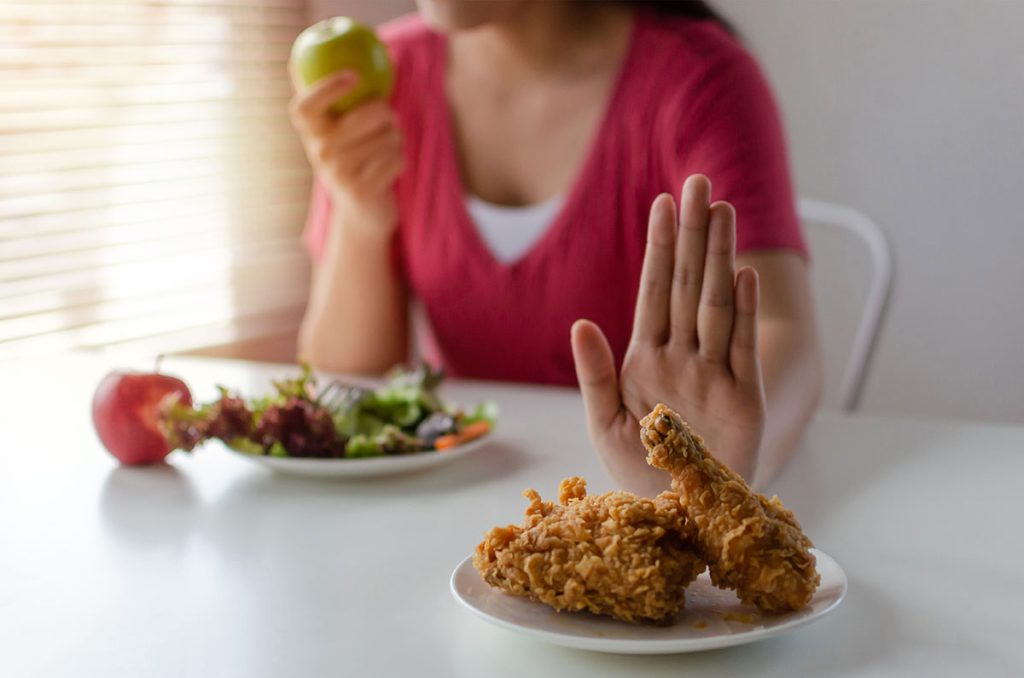 woman eating fruits and veggies and saying no to fried chicken