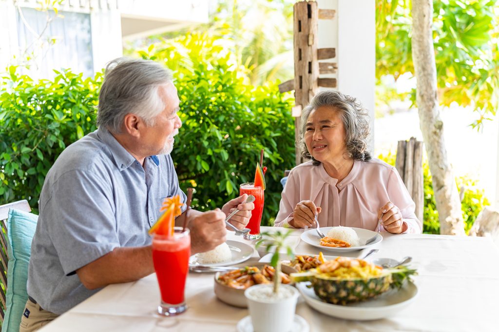 Happy family senior couple having lunch and sharing meal together at restaurant. Elderly people man and woman enjoy retirement with outdoor activity lifestyle on summer holiday travel vacation.