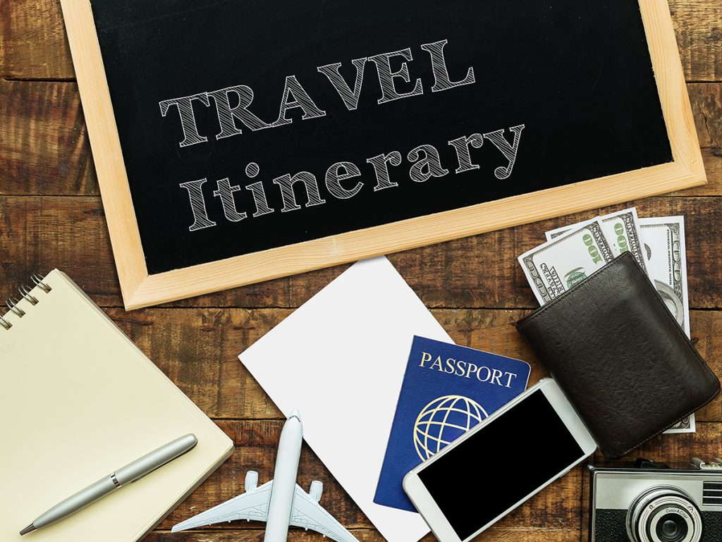travel itinerary handwritten with white chalk on a blackboard decorate with plane model, passport, money wallet , notebook , camera and smartphone on a wooden background