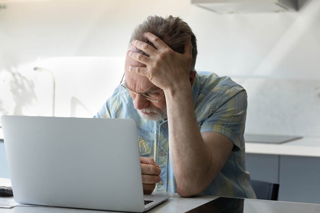 Frustrated tired senior man touching head at laptop