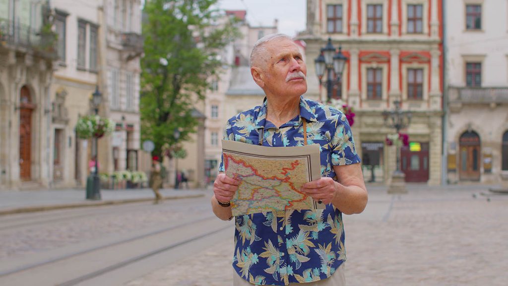 Elderly mature tourist man walking along street, confused looking at map