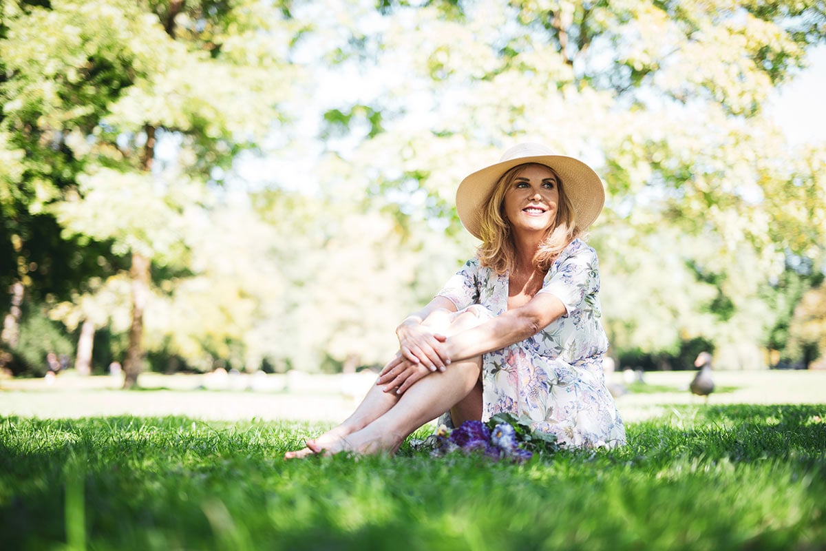 elder woman happy on grass in the sun with a hat