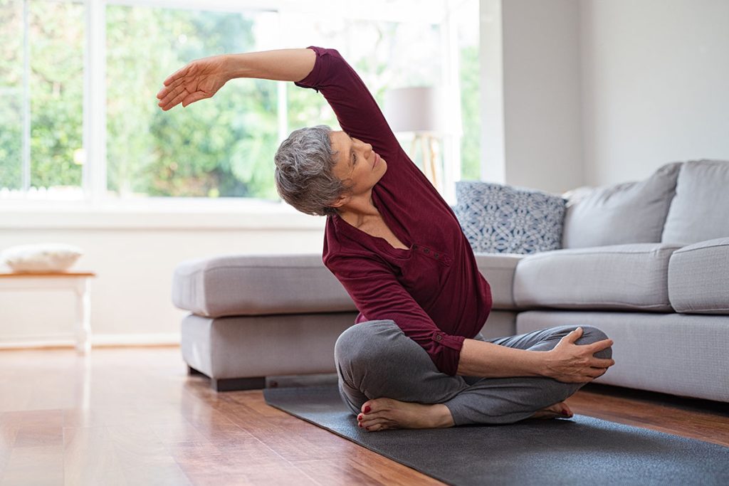 elder woman stretching on yoga mat in living room