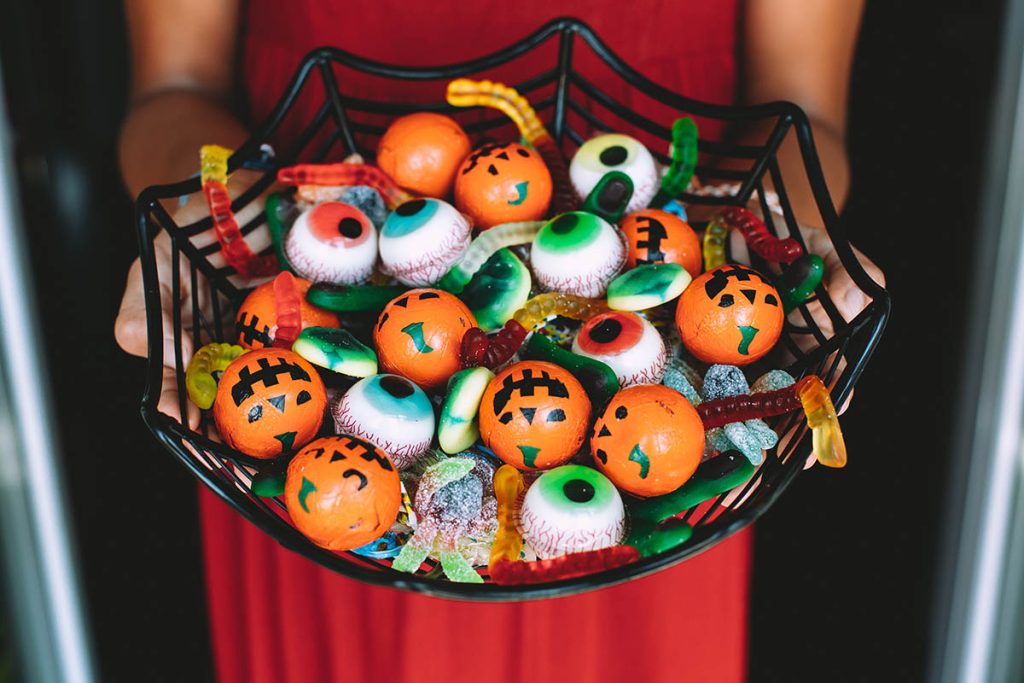 Woman at the front door offering funny Halloween candies on a spiderweb shaped bowl.