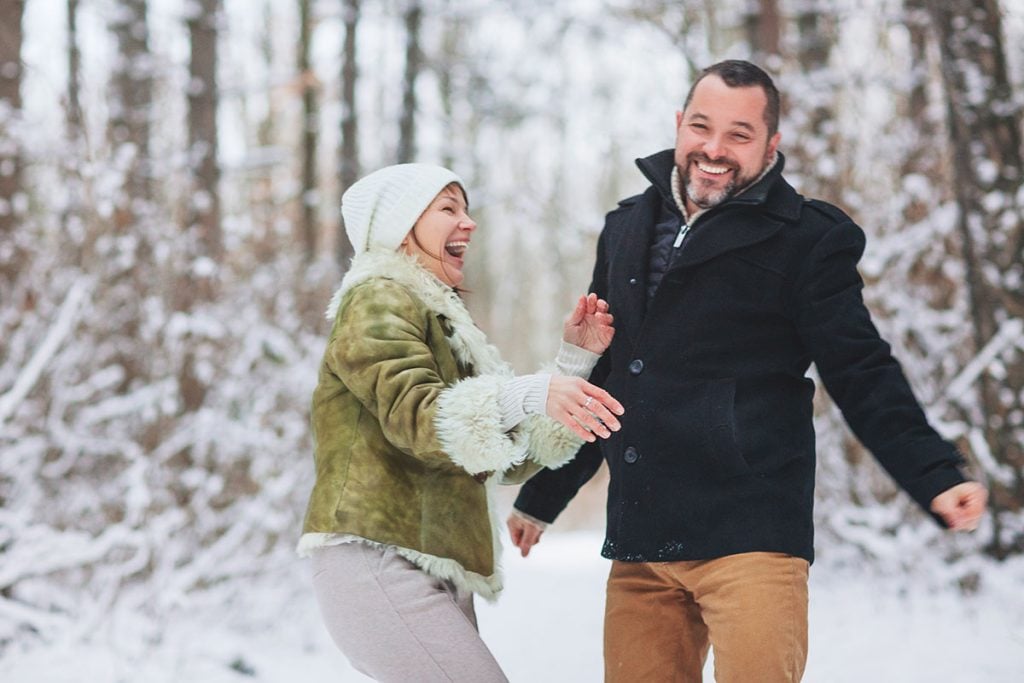 Lovely happy middle-aged family couple having fun outdoors in winter season vacation together, taking walk through snowy forest with smile, dressed in warm clothes. 