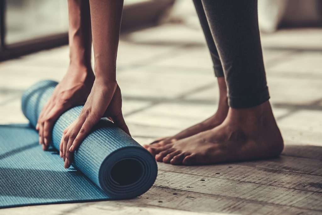 woman rolling up blue yoga mat