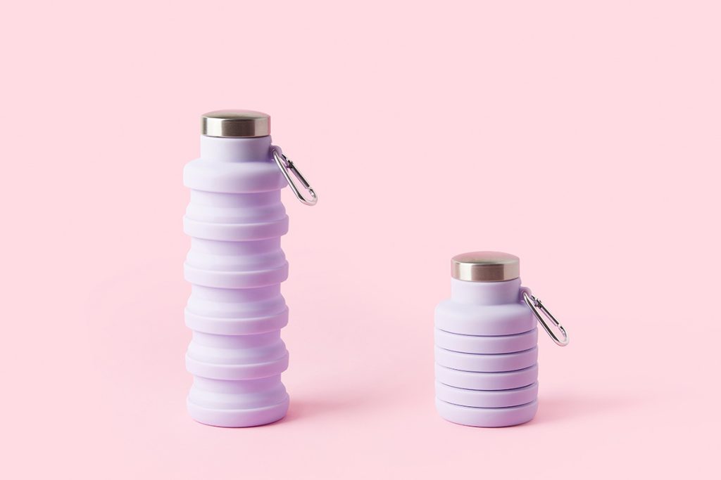 Collapsible reusable lilac water bottle on pink background. 